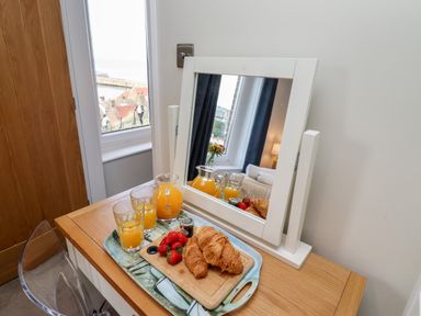 A wooden desk with a mirror on it and a tray with croissants strawberries and orange juice at Mariners Watch in Whitby