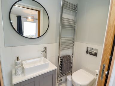 A bathroom with a circular mirror above a sink next to a towel rack and a toilet at Mariners Watch in Whitby