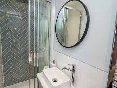A bathroom with a glass shower enclosure a rectangular sink a round mirror and wall tiles at Mariners Watch in Whitby