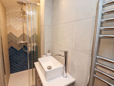A bathroom with a shower area with multicolored tiles a white sink with a chrome faucet a soap dispenser and a chrome towel radiator at Mariners Watch in Whitby