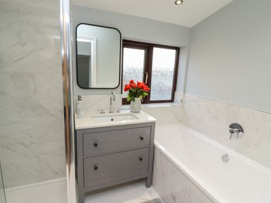 A bathroom with a bathtub a vanity with a sink a mirror and a window with frosted glass at Mariners Watch in Whitby