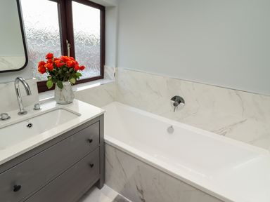 A bathroom with a white bathtub next to a sink with a faucet and a vase of red flowers on the counter at Mariners Watch in Whitby