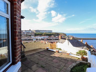 A patio area with paving stones overlooking a coastal town and harbor with buildings and the sea at Mariner's Watch in Whitby