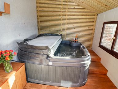 An indoor hot tub with a partially folded cover a bottle and glasses on the edge wooden steps and walls with a window and brick detail at Mariners Watch in Whitby