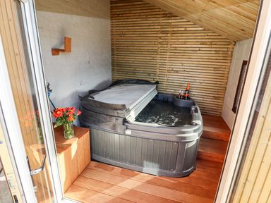 An indoor hot tub with partially removed cover wooden floor and walls flowers in a vase and a bottle with glasses at Mariners Watch in Whitby