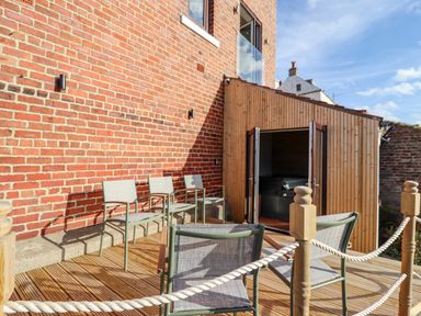 An outdoor patio area with chairs on a wooden deck next to a brick wall and a wooden structure with open doors at Mariners Watch in Whitby