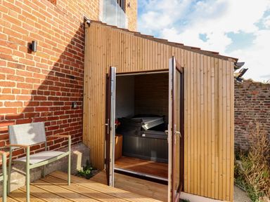 An outdoor wooden deck with a chair and an open wooden structure containing a covered hot tub at Mariners Watch in Whitby