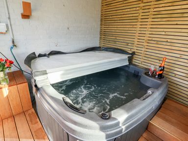 An indoor hot tub with partially open cover and a bottle with glasses on a wooden deck at Mariner's Watch in Whitby