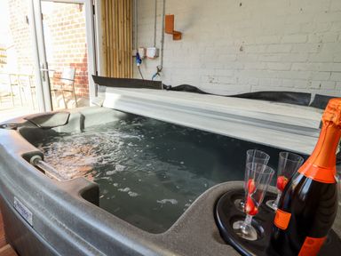 A hot tub with water and bubbles three glasses with strawberries and a bottle of sparkling drink indoors near glass doors at Mariners Watch in Whitby