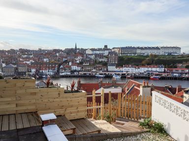 A view of a harbor with boats and buildings across the water from a wooden deck and fence at Mariners Watch in Whitby