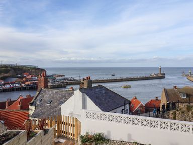 View over rooftops toward a harbor with piers and boats on the water at Mariners Watch in Whitby
