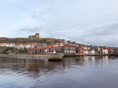 A coastal town with red roof houses a stone pier and a church on a hill at Mariners Watch in Whitby