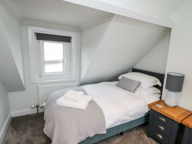 A small bedroom with a single bed beside a window and a wooden nightstand with a lamp at Mariners Watch in Whitby