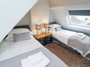 A bedroom with two single beds a nightstand with two lamps and a window at Mariners Watch in Whitby