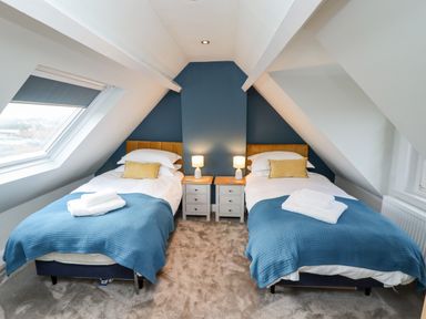 A bedroom with two single beds with blue blankets and yellow cushions a skylight window and bedside tables with lamps at Mariners Watch in Whitby