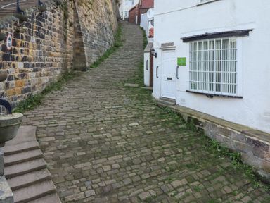A narrow cobblestone street between a stone wall and white buildings at Mariners Watch in Whitby