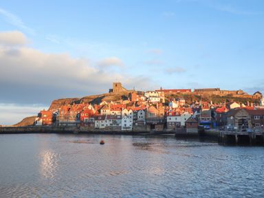 A coastal town with red and white buildings by the water and a historic church on a hill at Mariners Watch in Whitby