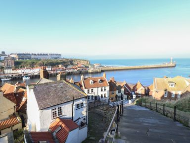 A coastal town with stairs leading down to houses and a harbor with a lighthouse at Mariners Watch in Whitby