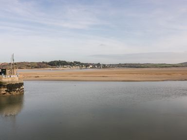A body of water with a small structure saying slow speed and a sandy shore with houses and green hills in the distance at Summer Breeze in Tregolds near St Merryn