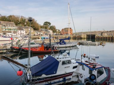 A harbor with several boats docked including sailboats and fishing boats with buildings and a hill in the background at Summer Breeze Tregolds near St Merryn