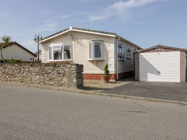 A single-story house with bay windows a stone wall and a garage with a white door at Summer Breeze in Tregolds near St Merryn
