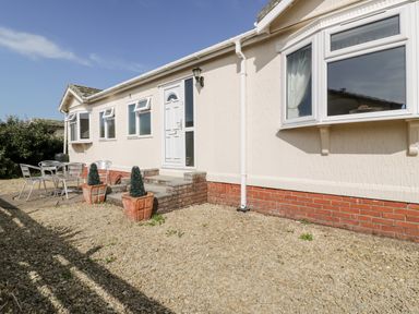 A gravel front yard with steps leading to a white door and metal patio furniture at Summer Breeze in Tregolds near St Merryn