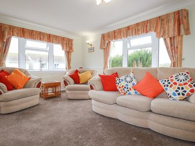 A living room with two beige armchairs and a beige sofa with cushions and curtains at Summer Breeze in Tregolds near St Merryn