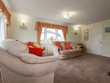 A living room with two beige sofas with colorful cushions and orange curtains at Summer Breeze in Tregolds near St Merryn