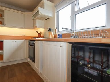 A kitchen with white cabinets oven stove knife block and window at Summer Breeze in Tregolds near St Merryn