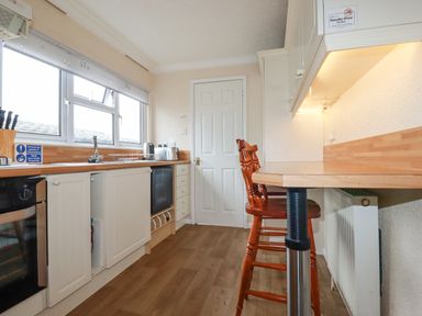 A kitchen with wooden countertops two wooden chairs a window and white cabinets at Summer Breeze in Tregolds near St Merryn