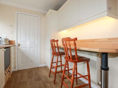 A kitchen with wooden stools at a counter and white cabinets at Summer Breeze in Tregolds near St Merryn