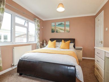 A bedroom with a bed with orange pillows and a yellow throw next to windows and a chest of drawers at Summer Breeze in Tregolds near St Merryn
