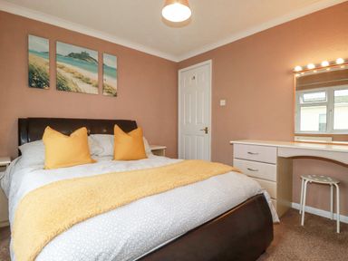 A bedroom with a bed with yellow pillows and blanket a dressing table with mirror and window at Summer Breeze Tregolds near St Merryn