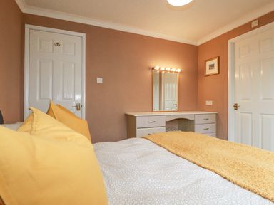 A bedroom with a bed featuring yellow pillows and blanket and a dressing table with mirror and lights at Summer Breeze in Tregolds near St Merryn