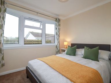 A bedroom with a bed with green pillows and an orange blanket near a window at Summer Breeze in Tregolds near St Merryn
