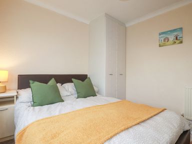 A bedroom with a bed green pillows a yellow blanket a bedside table with a lamp a wardrobe and a painting on the wall at Summer Breeze in Tregolds near St Merryn