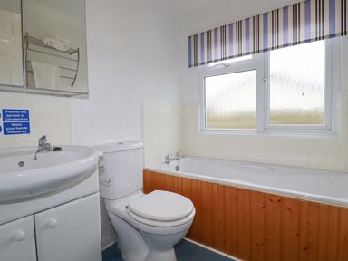 A bathroom with a sink cabinet toilet and bathtub under a window at Summer Breeze in Tregolds near St Merryn