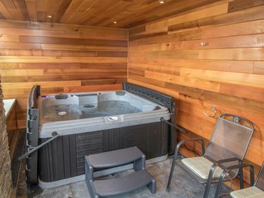 An indoor hot tub with water and black plastic steps next to metal chairs with cushions at Boathouse on the Lake in Bowness-On-Windermere