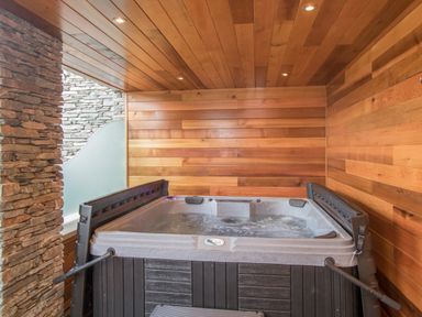 An indoor hot tub with wooden walls and ceiling and stone wall on one side at Boathouse on the Lake in Bowness-On-Windermere