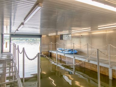 An indoor boat storage area with water and a blue kayak on a metal platform at Boathouse on the Lake in Bowness-On-Windermere