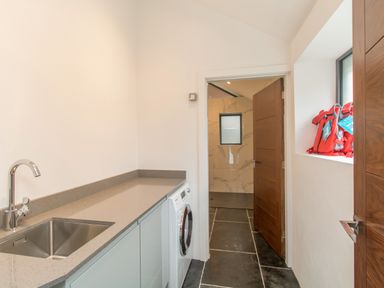 A laundry room with a sink washing machine countertop open door and life jackets on a window ledge at Boathouse on the Lake in Bowness-On-Windermere