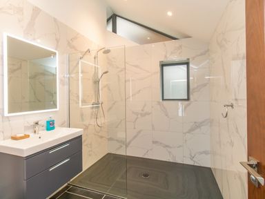A bathroom with a wall-mounted sink and mirror next to a walk-in shower at Boathouse on the Lake in Bowness-On-Windermere