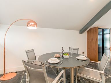 A dining area with a round table set for three with bowls plates wine glasses and a salad bowl with a floor lamp and a wooden cabinet at Boathouse on the Lake in Bowness-On-Windermere