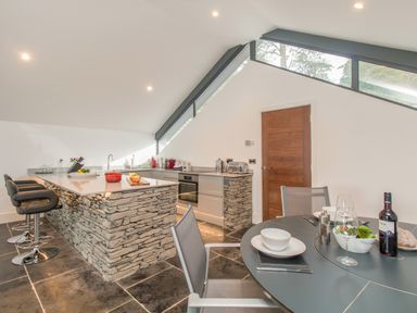 A kitchen with a stone island and bar stools next to a dining table with chairs and food at Boathouse on the Lake in Bowness-On-Windermere