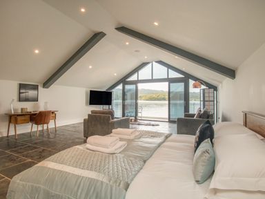 A bedroom with a bed and seating area overlooking a lake at Boathouse on the Lake in Bowness-On-Windermere