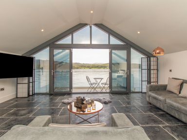 A living room with sofas a round coffee table and large glass doors opening to a lake view at Boathouse on the Lake in Bowness-On-Windermere