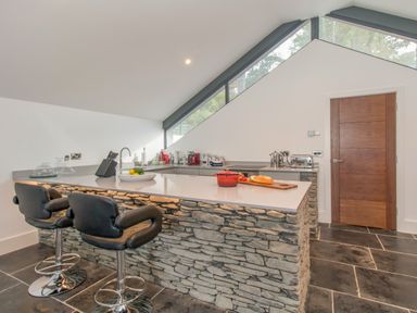 A kitchen with a stone island counter and two black bar stools at Boathouse on the Lake in Bowness-On-Windermere