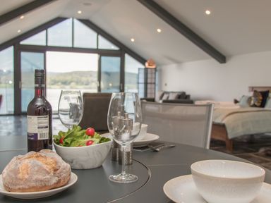 A table set with bread salad wine glass and bowl in a room with a bed and large windows at Boathouse on the Lake in Bowness-On-Windermere