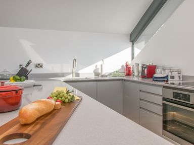 A kitchen with a countertop holding bread, grapes, and cheese near a sink and built-in oven at Boathouse on the Lake in Bowness-On-Windermere