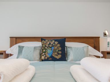 A bed with a wooden headboard with patterned cushions and white towels in a bedroom at Boathouse on the Lake in Bowness-On-Windermere